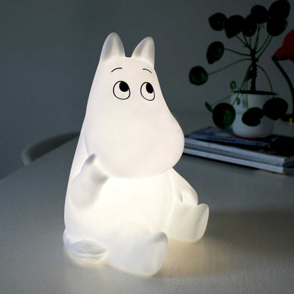 Sitting Moomin lamp lit up on a table beside a plant
