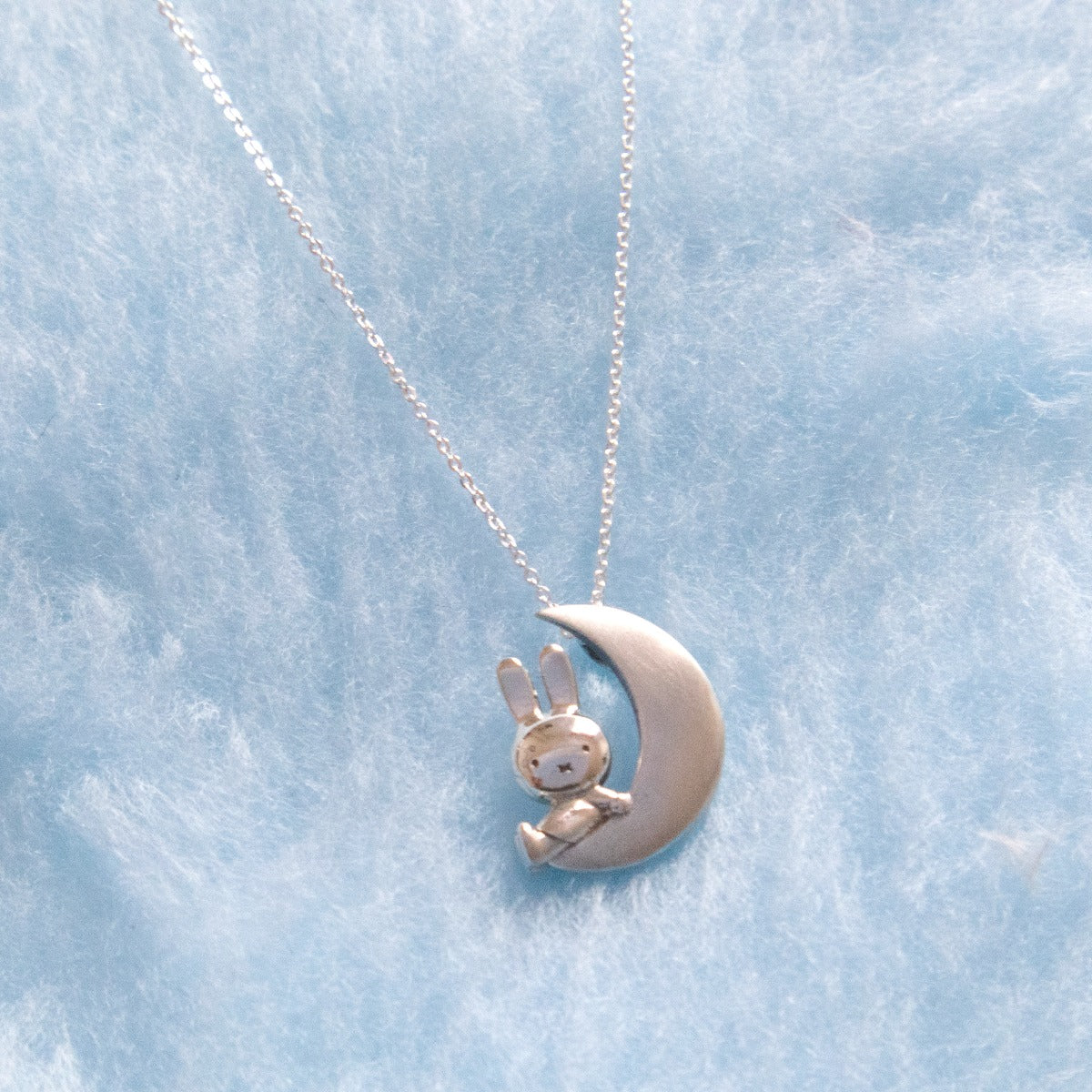 Miffy sitting on a crescent moon pendant on blue fur