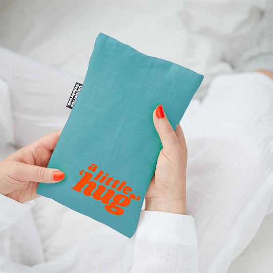 Hands holding a blue linen hot water bottle cover with 'A little hug' in orange