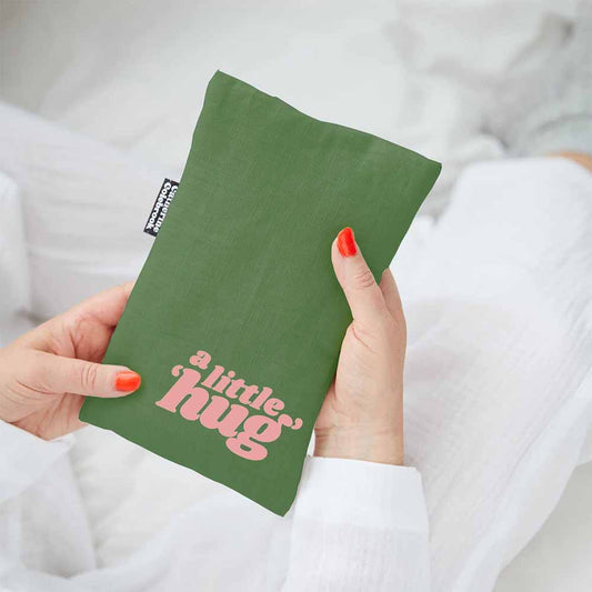 Hands holding a green linen hot water bottle cover with 'A little hug' in pink