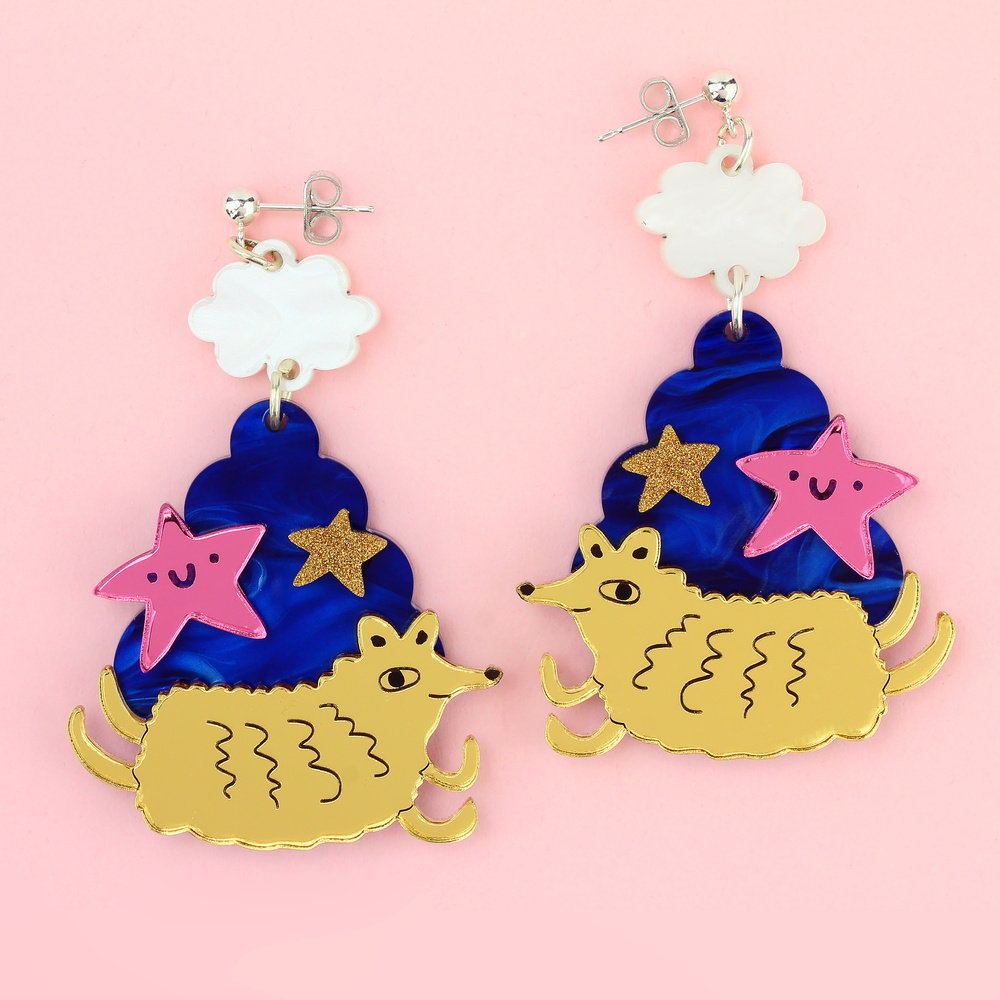 Drop earrings with a white cloud stud, a gold hedgehog-like creature and pink and gold stars on a blue swirl