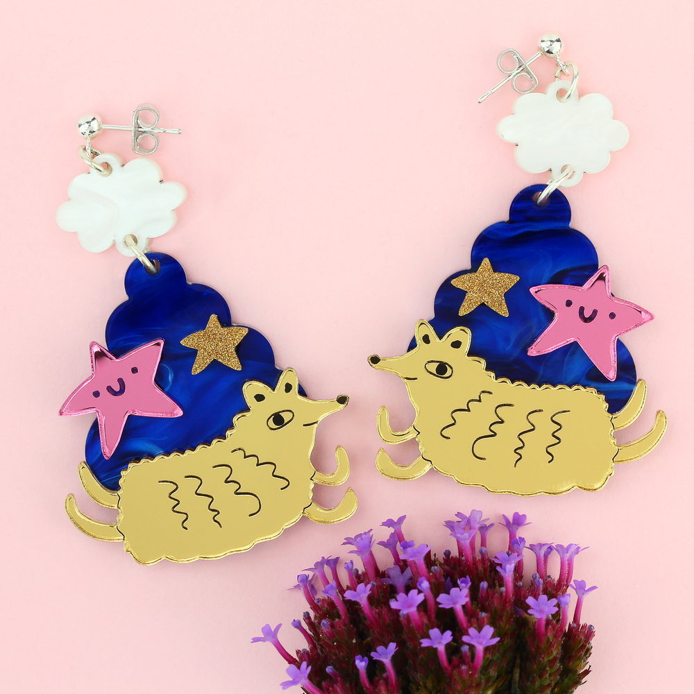 Cloud creature earrings beside purple flowers