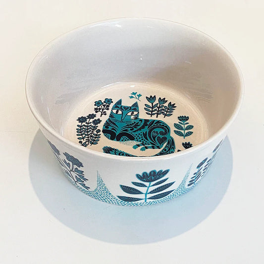 White ceramic bowl painted with a turquoise patterned cat among flowers, with a leaf border outside