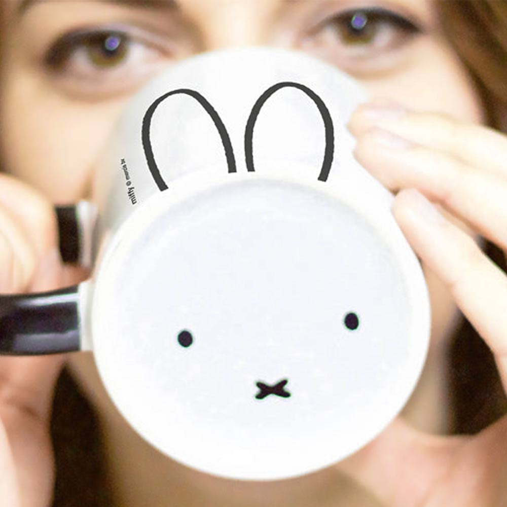 Woman drinking from a white Miffy mug that shows Miffy's face on the bottom