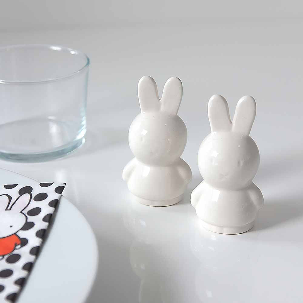 Miffy salt and pepper shakers on a white table beside a glass
