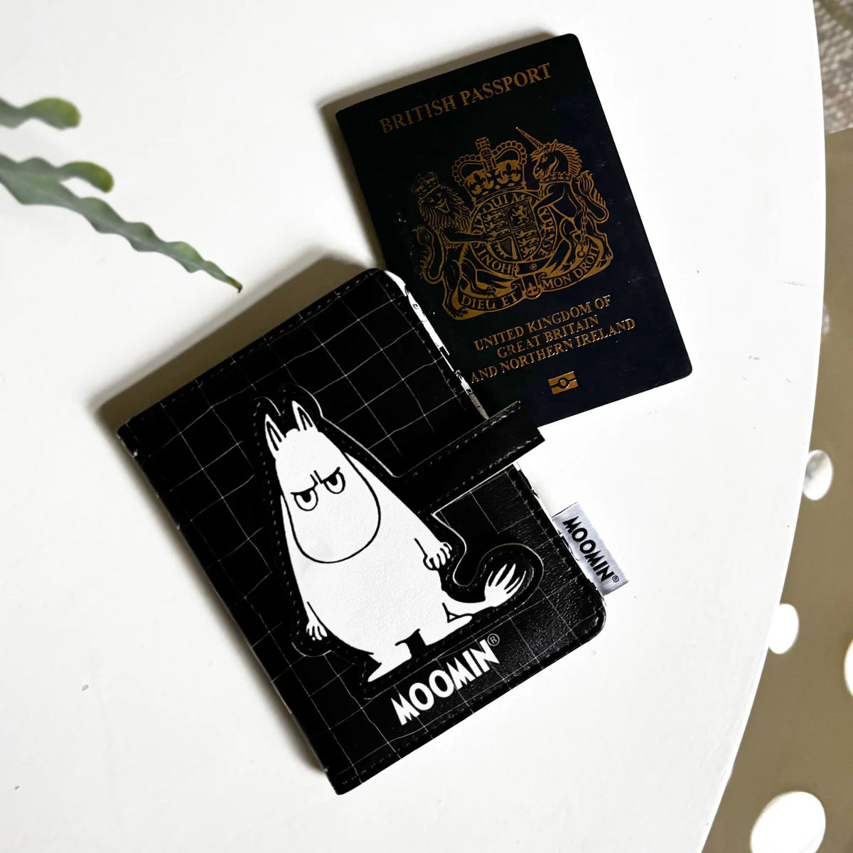 Black Moomin passport holder with an angry Moomintroll, beside a British passport
