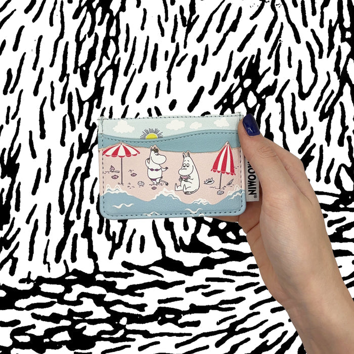 Hand holding the Moomin beach card holder against a black and white background