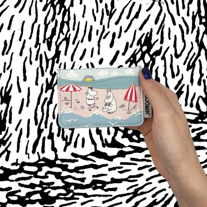 Hand holding the Moomin beach card holder against a black and white background