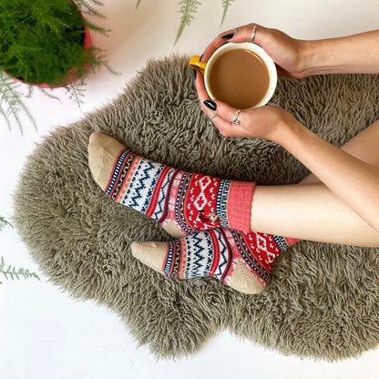 Person in Little My Fair Isle socks on a sheepskin, holding a coffee