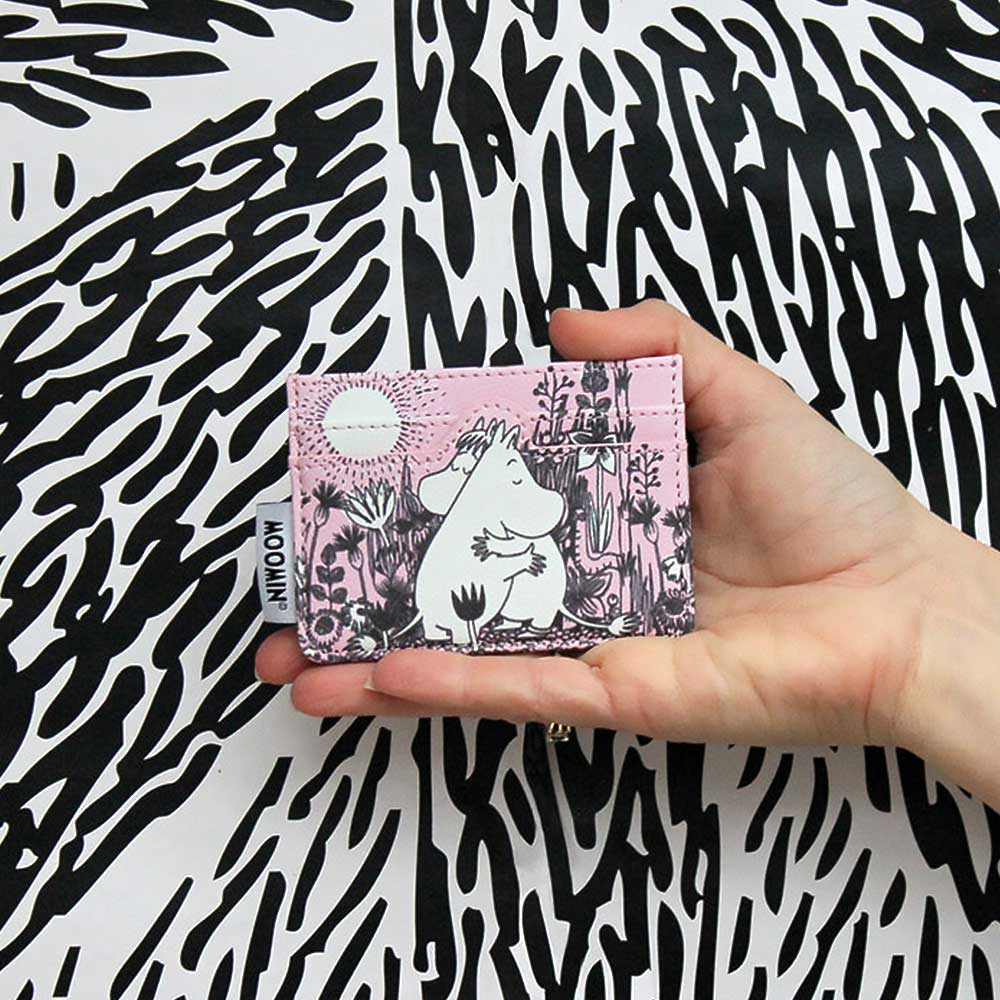 Hand holding the pink Moomin Love card holder against a black and white pattern