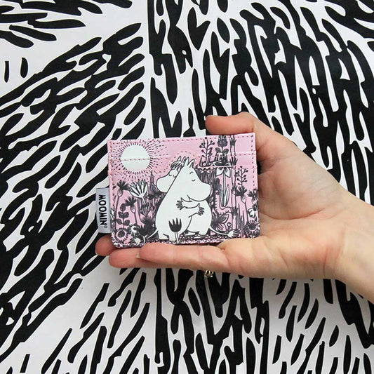 Hand holding the pink Moomin Love card holder against a black and white pattern