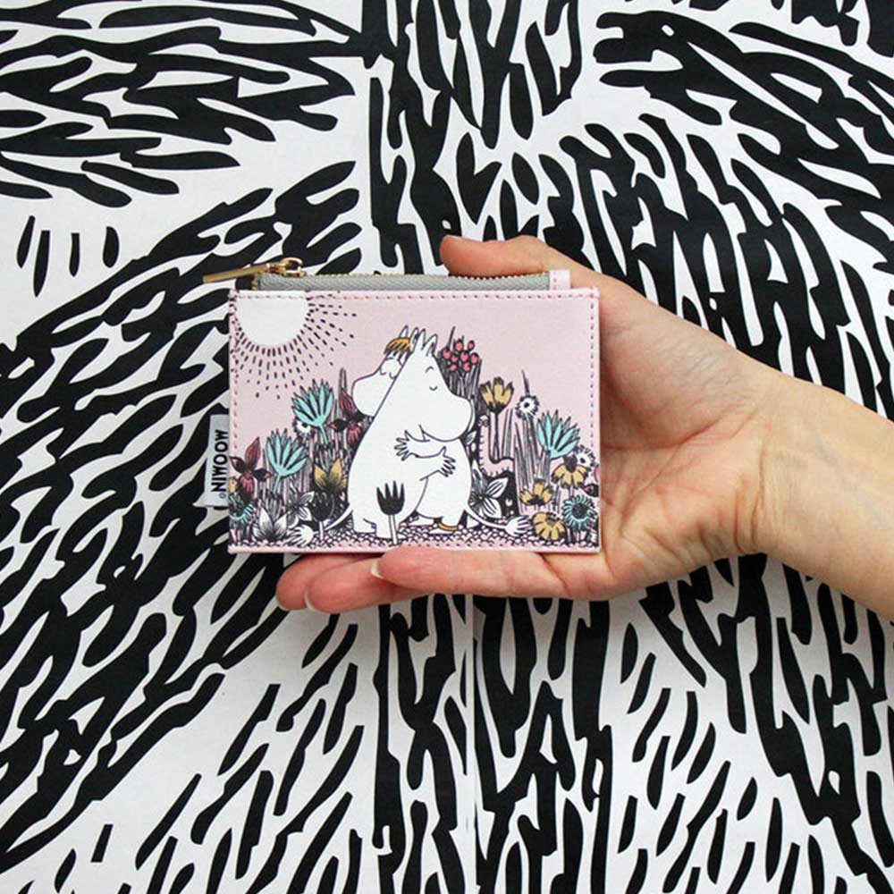 Hand holding the pink Moomin Love purse with Moomins hugging among flowers