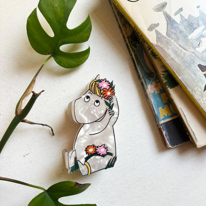 Pearly white Snorkmaiden hair claw with pink and red flowers, on a table beside a Moomin book