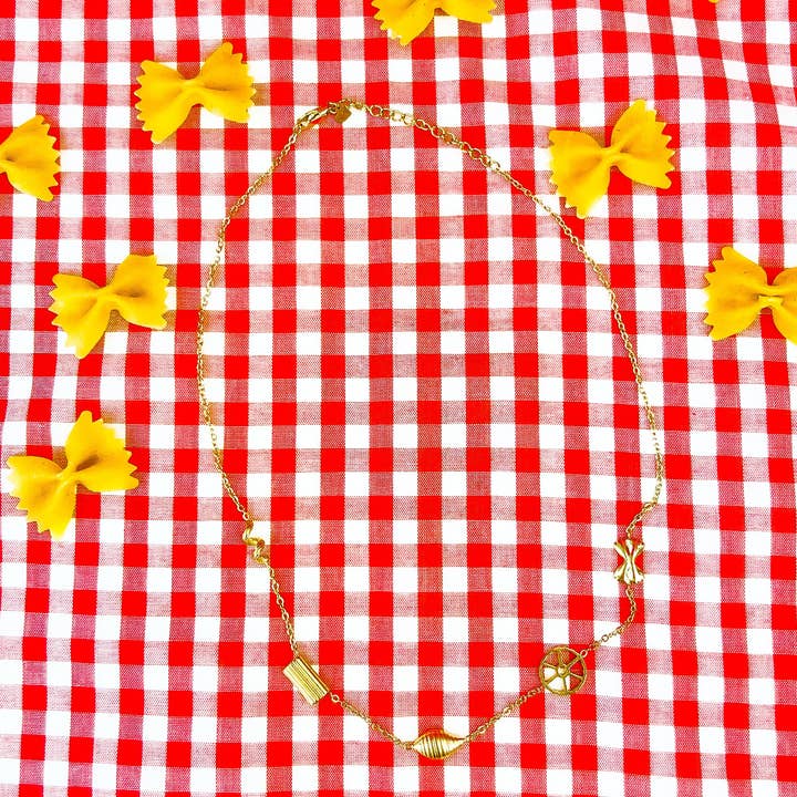 Gold pasta shape necklace among farfalle on red gingham
