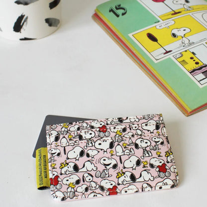 Patterned back of the pink Snoopy card holder holding a card, beside a Peanuts comic book
