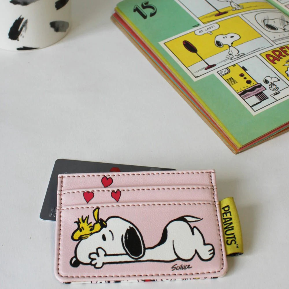 Pink Snoopy and hearts card holder holding a card, in front of a Peanuts comic book