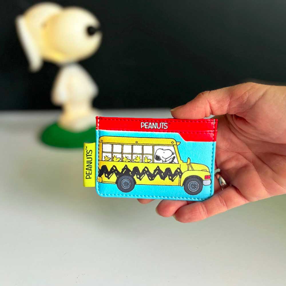 Hand holding the Peanuts school bus card holder in front of a Snoopy figure