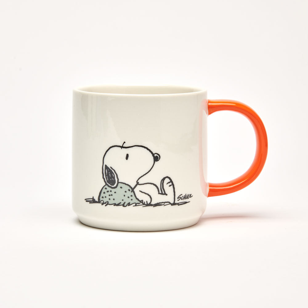 White mug with an orange handle and Snoopy lying on a rock