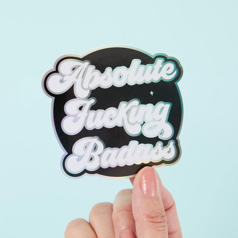 Punky Pins holographic sticker reading 'Absolute fucking badass', held in a hand