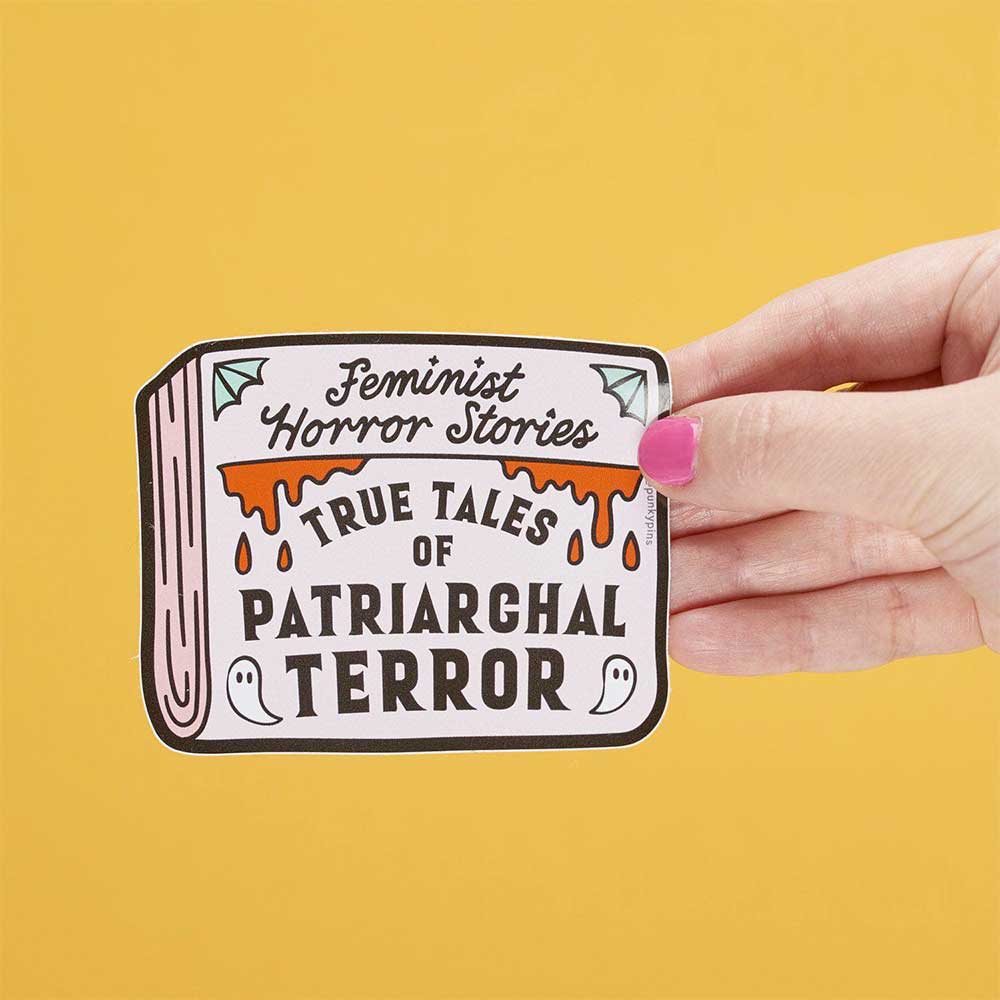 Hand holding a book-shaped sticker: Feminist horror stories, true tales of patriarchal terror
