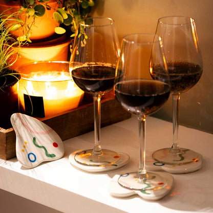 Belen coasters under glasses of red wine beside a candle