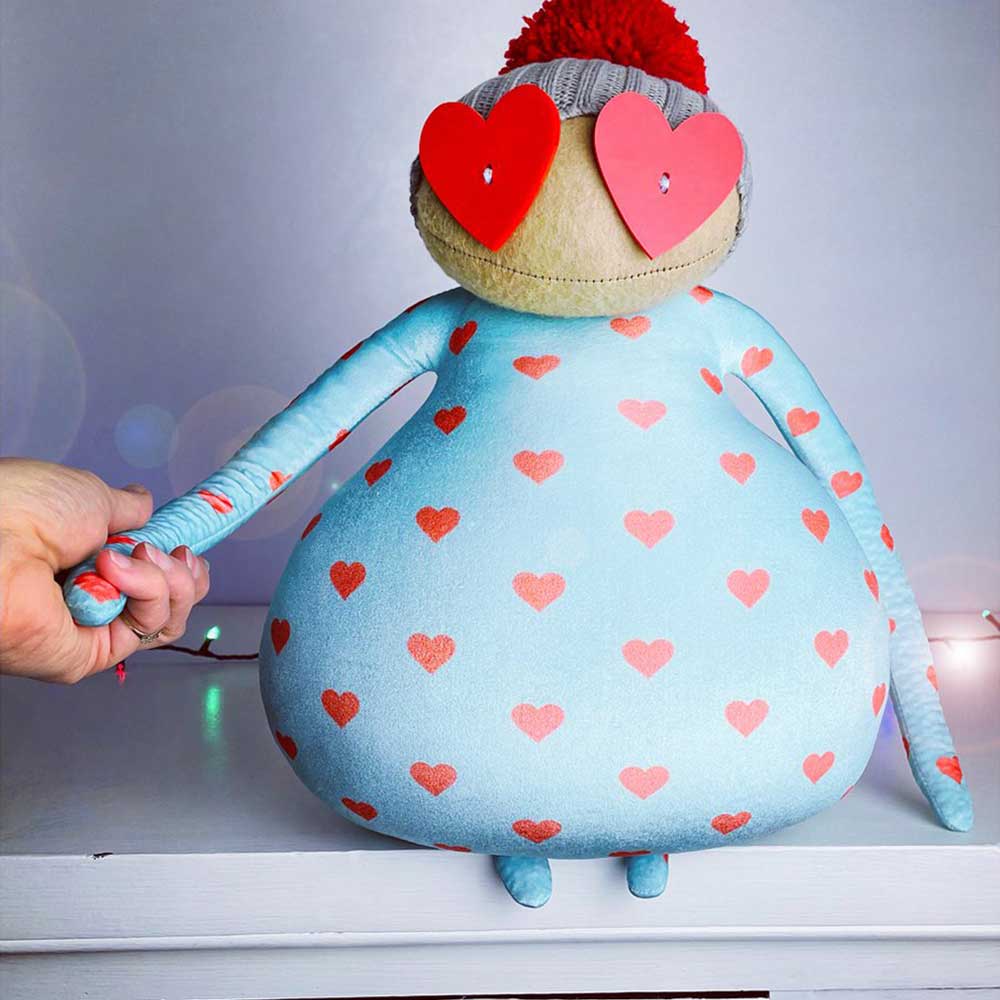 Ruby Ruth Ron soft toy: a pale blue heart-print creature with heart-shaped glasses and a red bobble hat