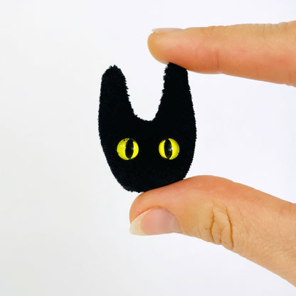 Ruby Ruth Jasper brooch: a fuzzy black cat head with yellow eyes, held between fingers