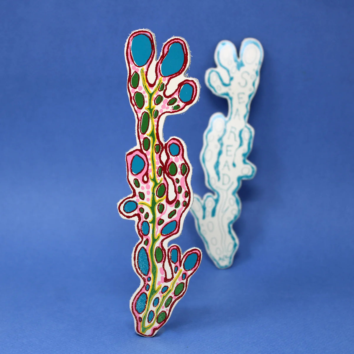 Pair of leather seaweed bookmarks, one cream with turquoise and pink spots, one pale blue