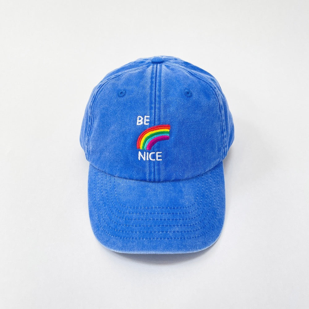 Blue washed cotton cap with a rainbow and 'Be nice' embroidered