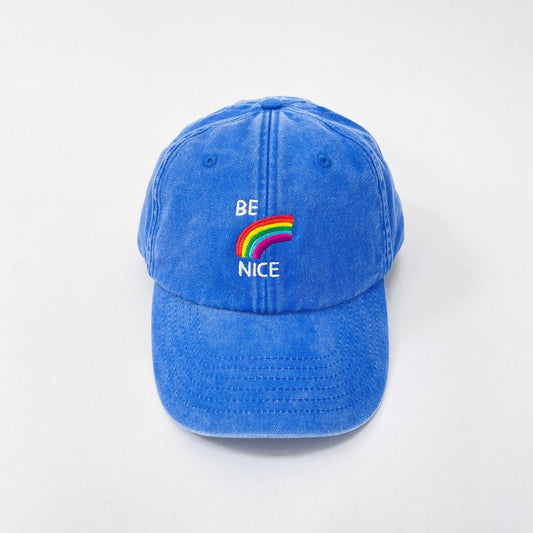 Blue washed cotton cap with a rainbow and 'Be nice' embroidered