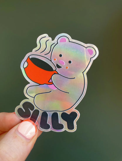 Naomi Wilkinson holographic sticker: a bear holding a red mug, with 'Silly'