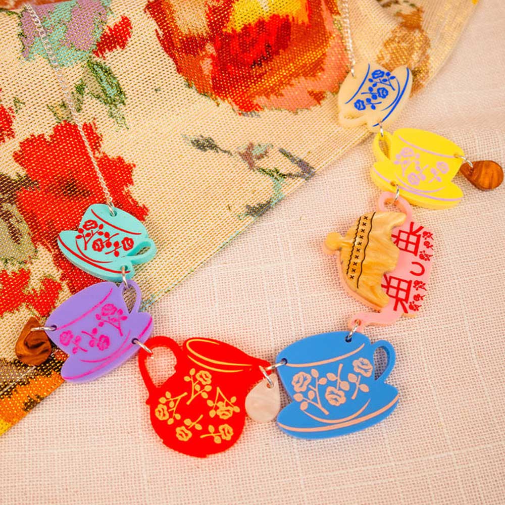 Cottage tea set necklace laid on a floral cloth