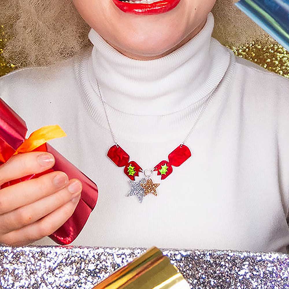 Woman in a white polo neck wearing the cracker necklace, holding a cracker