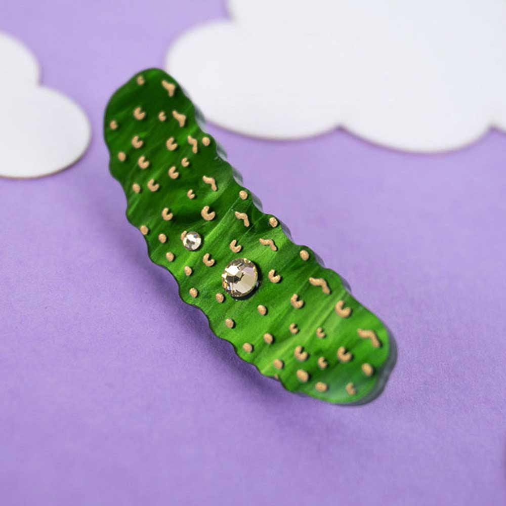 Pickle brooch on a lilac background with paper clouds