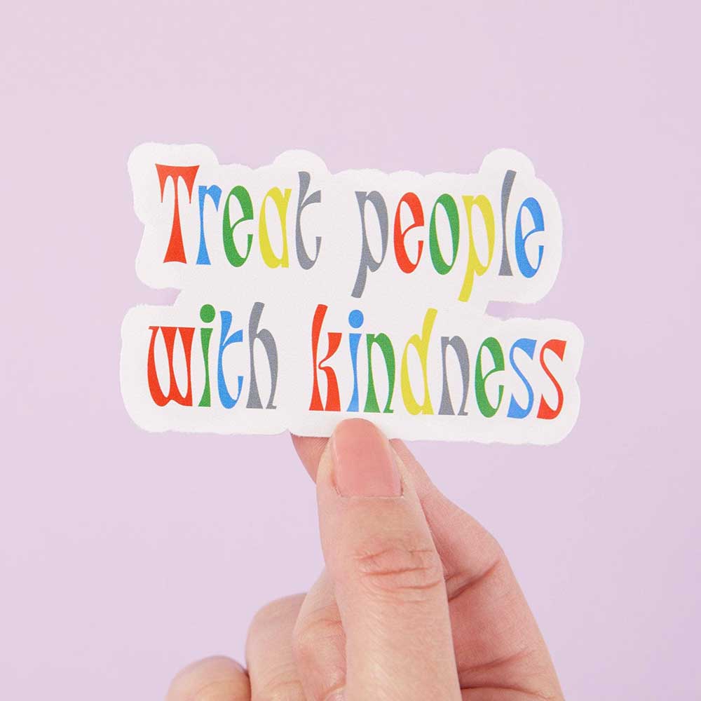 Hand holding a rainbow lettered sticker: Treat people with kindness
